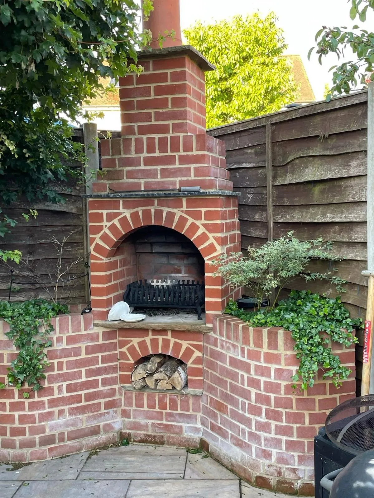 Brick-built outdoor fireplace with an arched opening and log store, by Cambourne Brickwork & Building