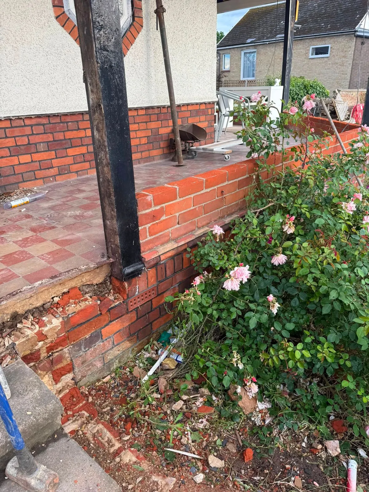 Red brick planter wall with climbing roses beside a tiled porch, by Cambourne Brickwork & Building