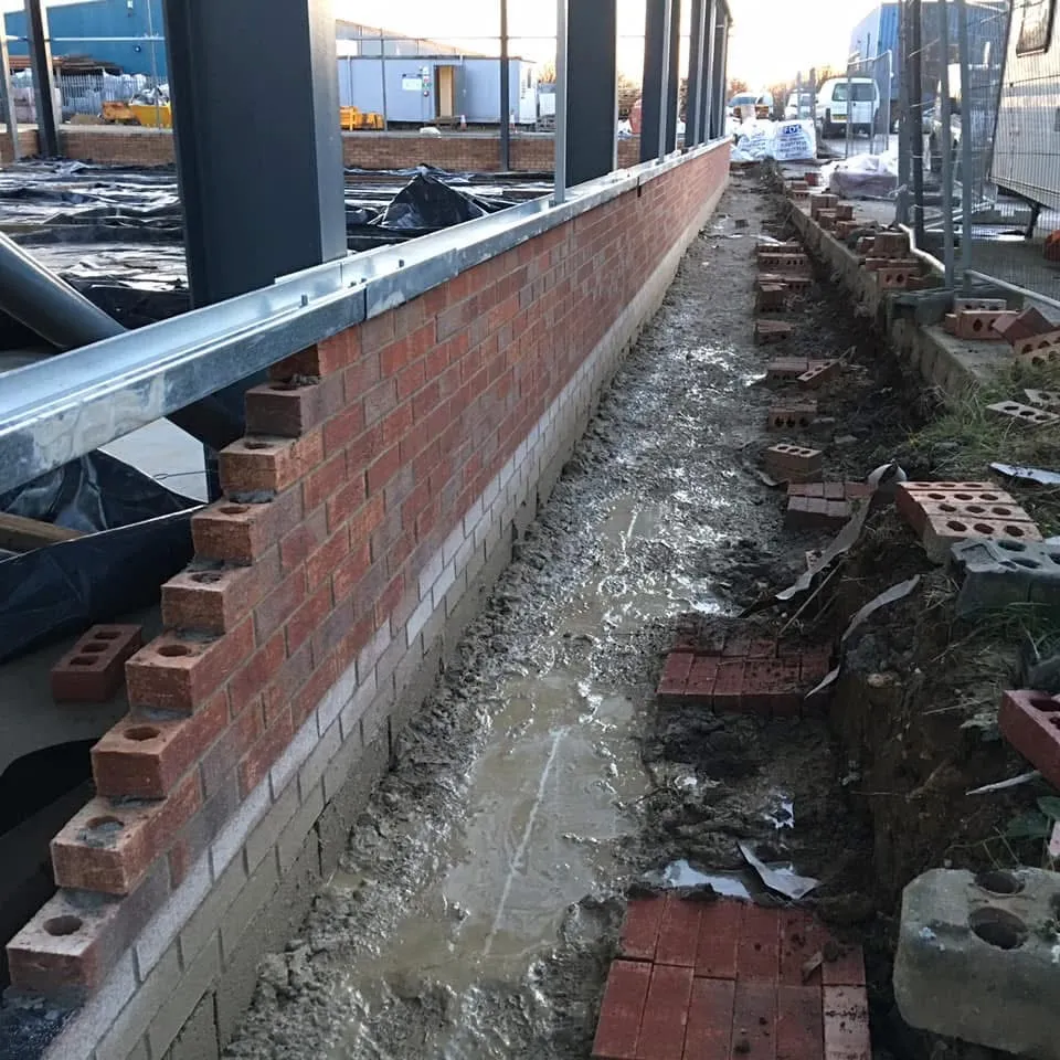 A long new-build brick wall alongside a foundation trench, by Cambourne Brickwork & Building